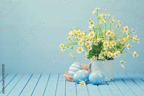 Easter holiday decoration with daisy flowers and painted eggs on wooden blue table