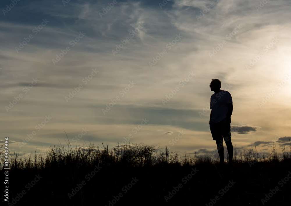 Man in silhouette standing on hill contemplating life and enjoying the view Man in silhouette standing on hill contemplating life and enjoying the view