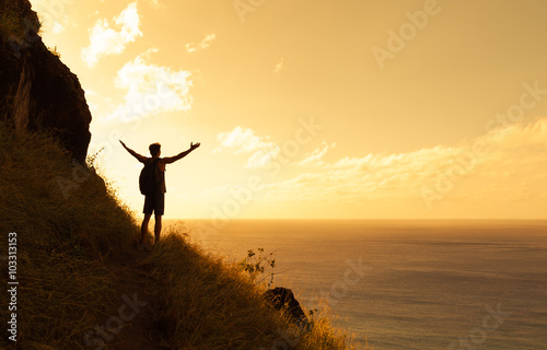 Happy man on top a mountain reaching his army out toward the horizon. Healthy lifestyle and life achievement concept.  photo