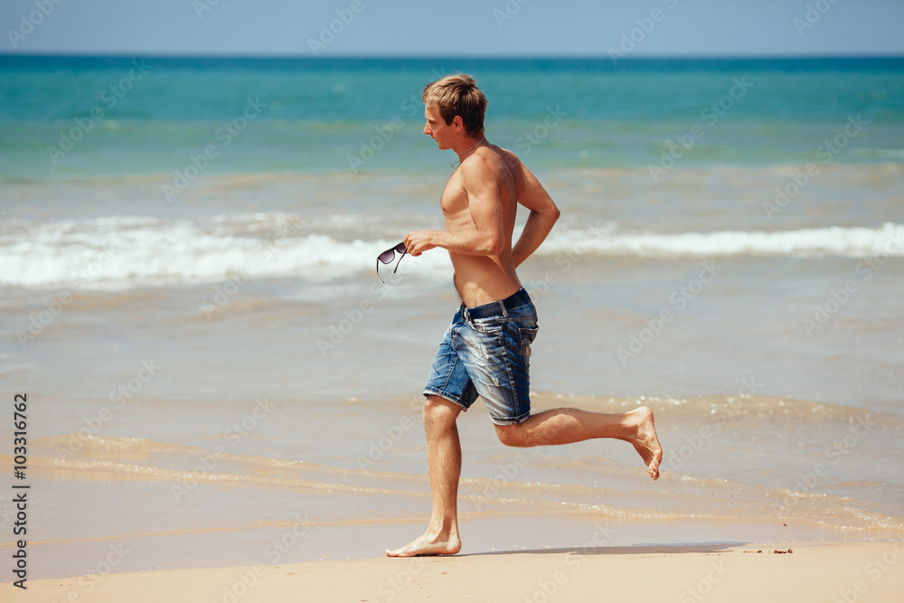 Man running on the beach with the sea in the background. Male ru