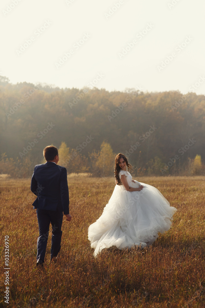 Happy newlywed couple run & pose in romantic sunset field