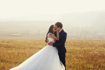 Romantic fairytale newlywed couple hug & smile in field at sunse