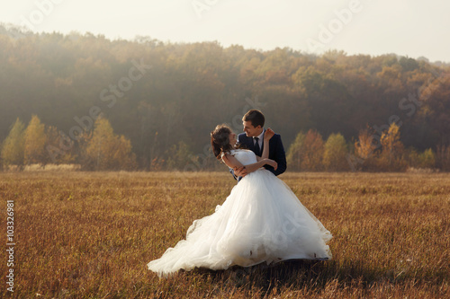 Romantic fairytale newlywed couple hug in field at sunset