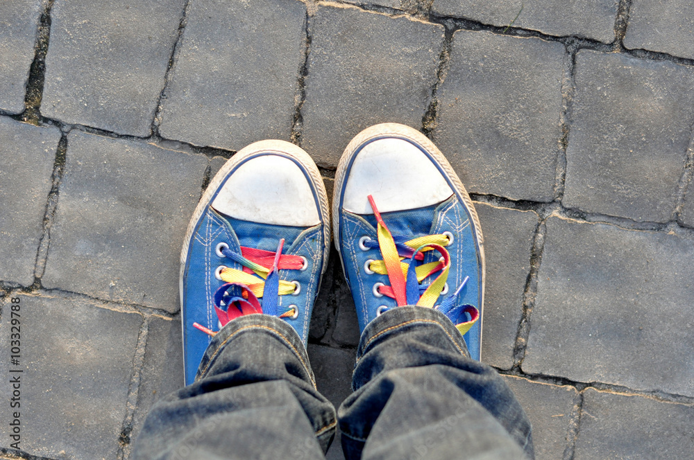 blue sneakers with colorful laces on pavement