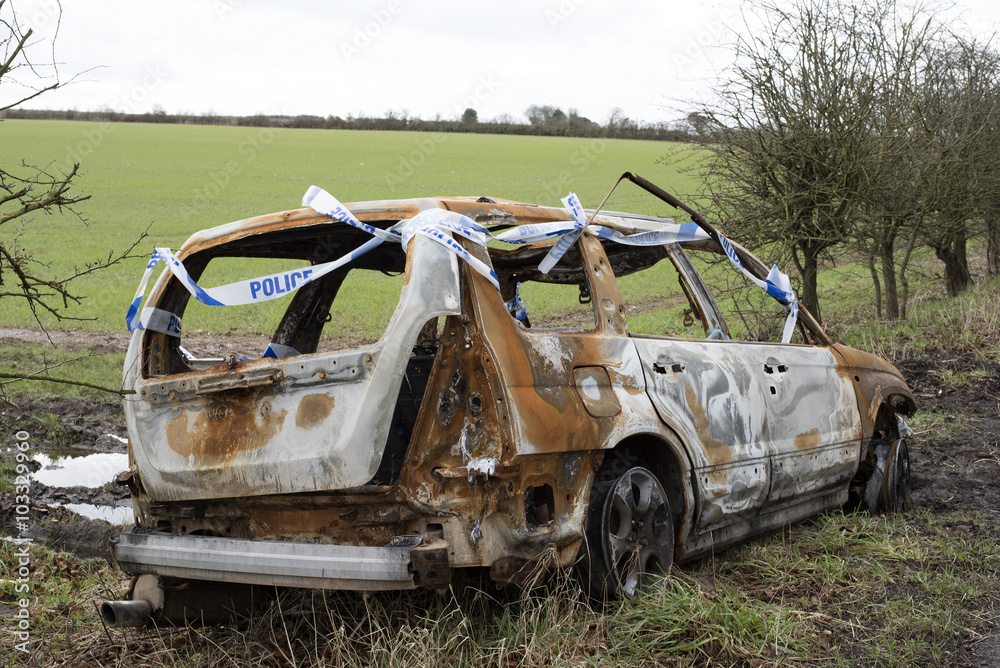 Burned out car and police tape in open countryside Burned out car and police tape in open countryside