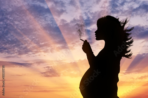 Silhouette of a pregnant woman smokes a cigarette