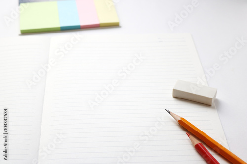 Blank notebook with pencil, red pencil, tag papers, and eraser on white background. 