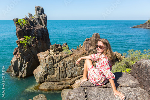 Young woman sitting on coastal rocks of Koh Chang island in Thailand.