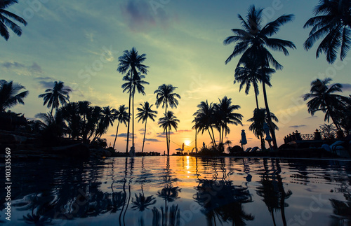 Beautiful sunset on a tropical beach with palm trees reflection in the water. © De Visu