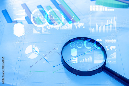 Magnifying glass and documents with analytics data lying on tabl