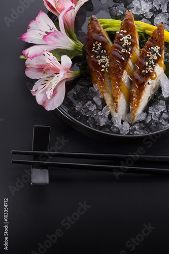 Eel sashimi with ice on a black plate with ginger wasabi over black background