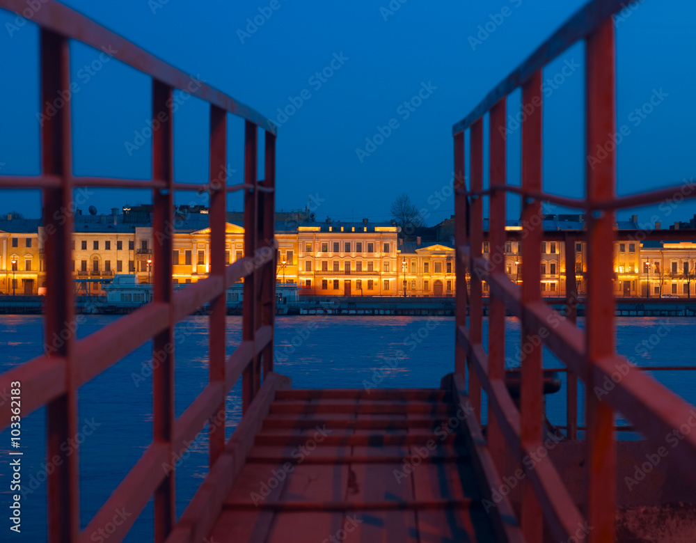 Fototapeta premium View of Neva and English embankment in St. Petersburg with night illumination through gangway on pier