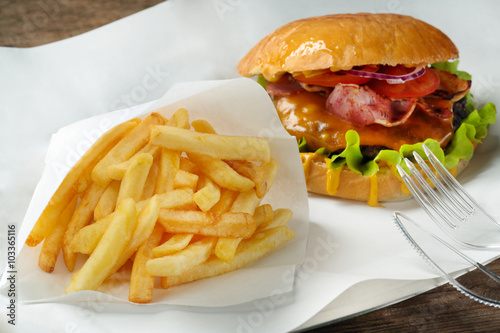 A burger, fries and fork with knife on paper