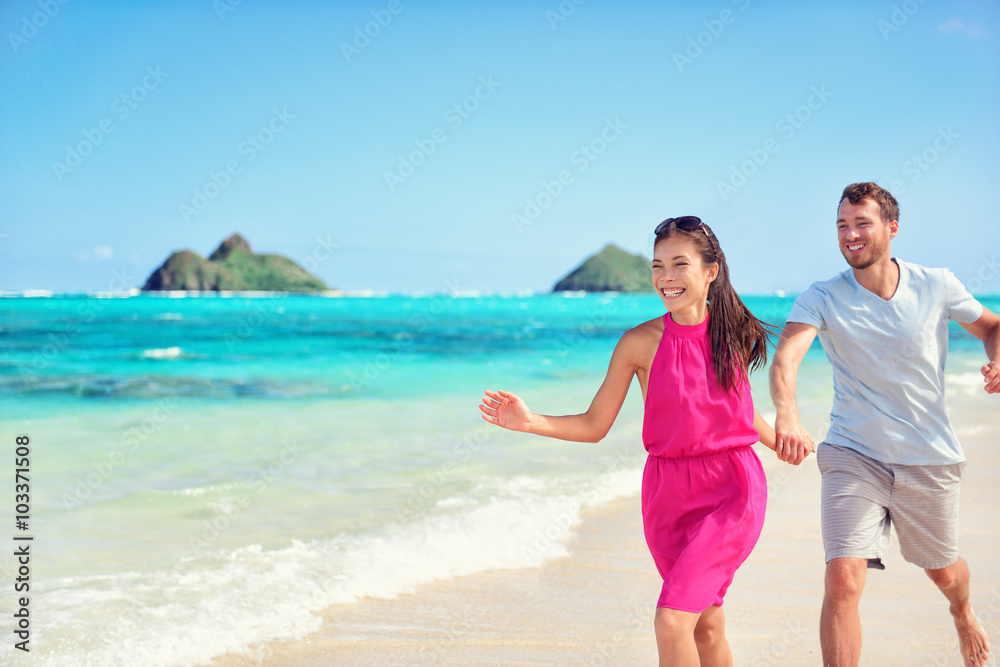 Happy multiracial Asian Caucasian couple having fun walking on perfect turquoise Lanikai Hawaii beach for summer vacation on Hawaiian island, Oahu, USA.