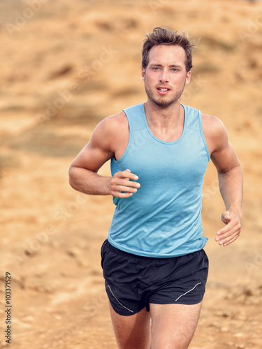 Trail runner training cardio running on rocky mountains yellow sand path in nature. Caucasian male athlete waist up portrait jogging living an active healthy lifestyle exercising outdoors.