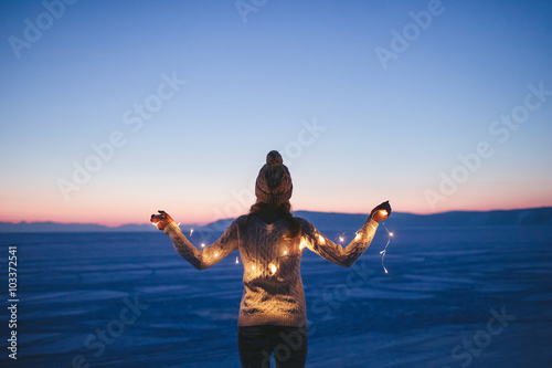 Girl with flashlights standing at the frozen lake at sunset in the evening  not in focus