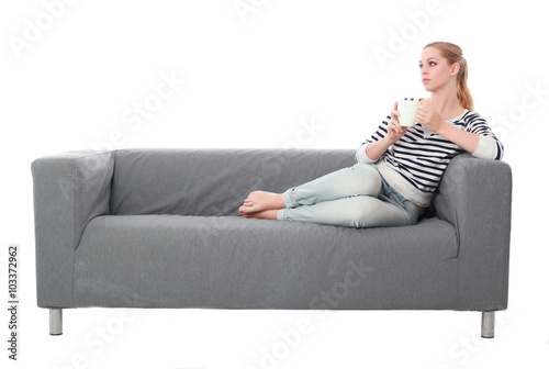 a pretty blonde lady wearing casual clothes, lounging on a grey sofa. isolated on a white background.