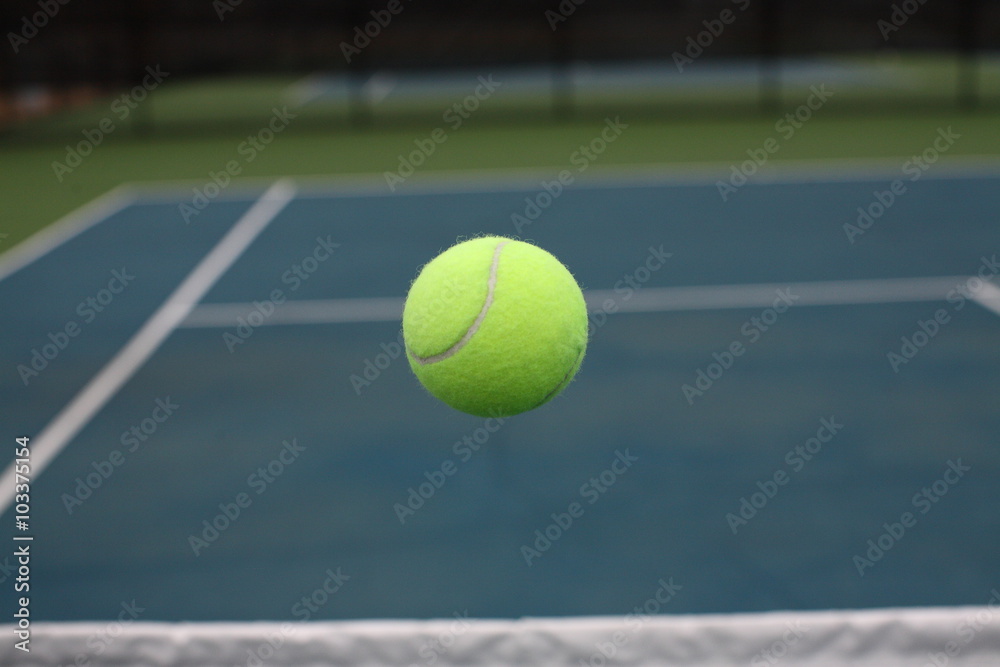 Tennis Ball Flying in Mid Air over Net on Blue Green Court