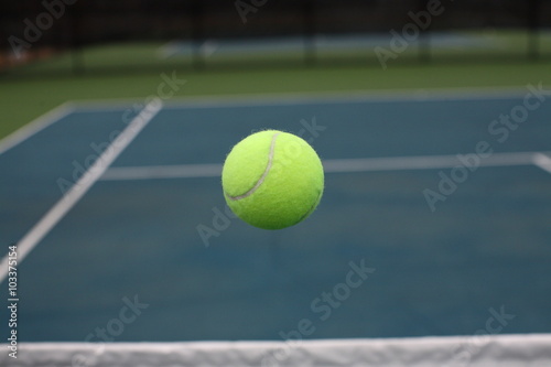 Tennis Ball Flying in Mid Air over Net on Blue Green Court