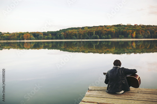 Young man playing on guitar at the lake