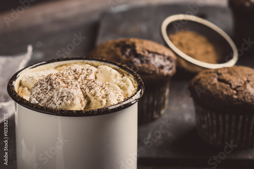 Cup of hot cocoa with marshmallows and chocolate muffins on the dark rustic wooden background. Toned image.