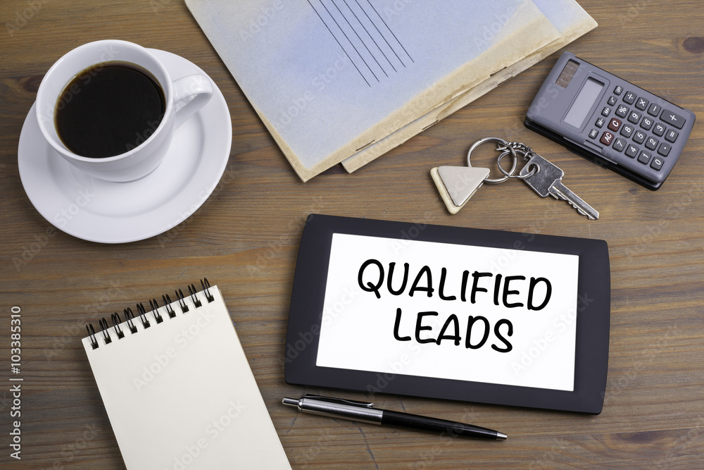 Qualified Leads. Text on tablet device on a wooden table Qualified Leads. Text on tablet device on a wooden table