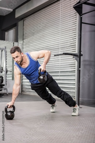 Muscular man doing push up with kettlebells