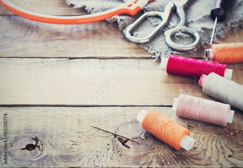 Scissors, bobbins with thread and needles, striped fabric. Old sewing tools on the old wooden background. Vintage Background