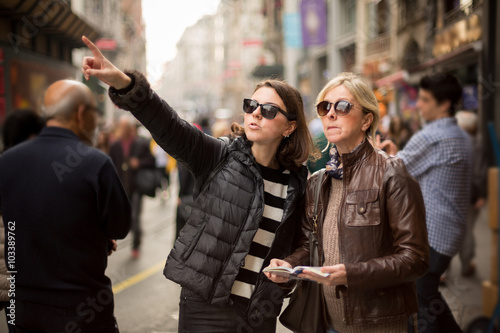 Mother and daughter are on the street and looking for a place to visit ,they are using a travel guide to explore where they travel photo