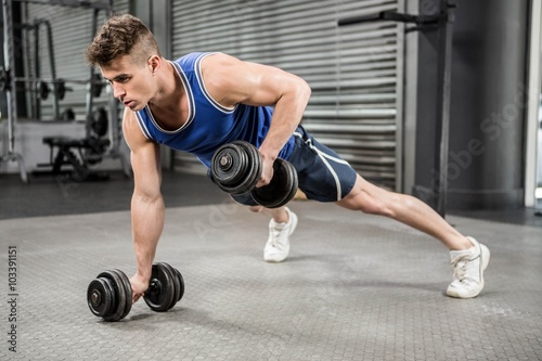 Muscular man doing push up with dumbbells