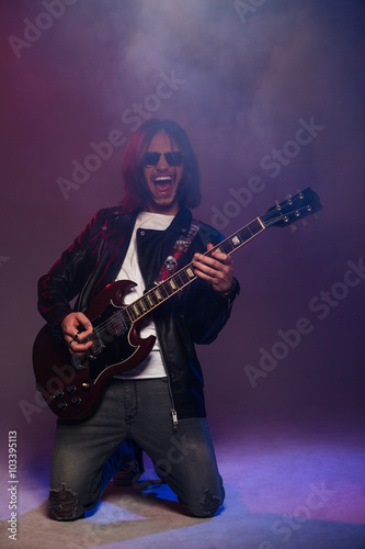 Happy male guitarist standing on knees and playing electric guitar