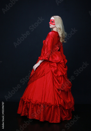 full length portrait of a beautiful blonde woman wearing a historical red silk, victorian era ball gown.