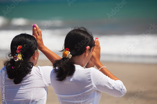 Two asian women with praying hands on ocean beach at ceremony Melasti before Balinese New Year and silence day Nyepi. Holidays, festivals, rituals, art, culture of Indonesian people and Bali island. photo