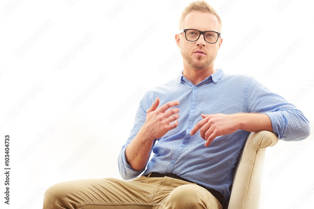 Fototapeta premium Talking young man. Portrait of handsome young man in casual blue shirt and dioptrical glasses sitting in comfortable pose isolated on white background