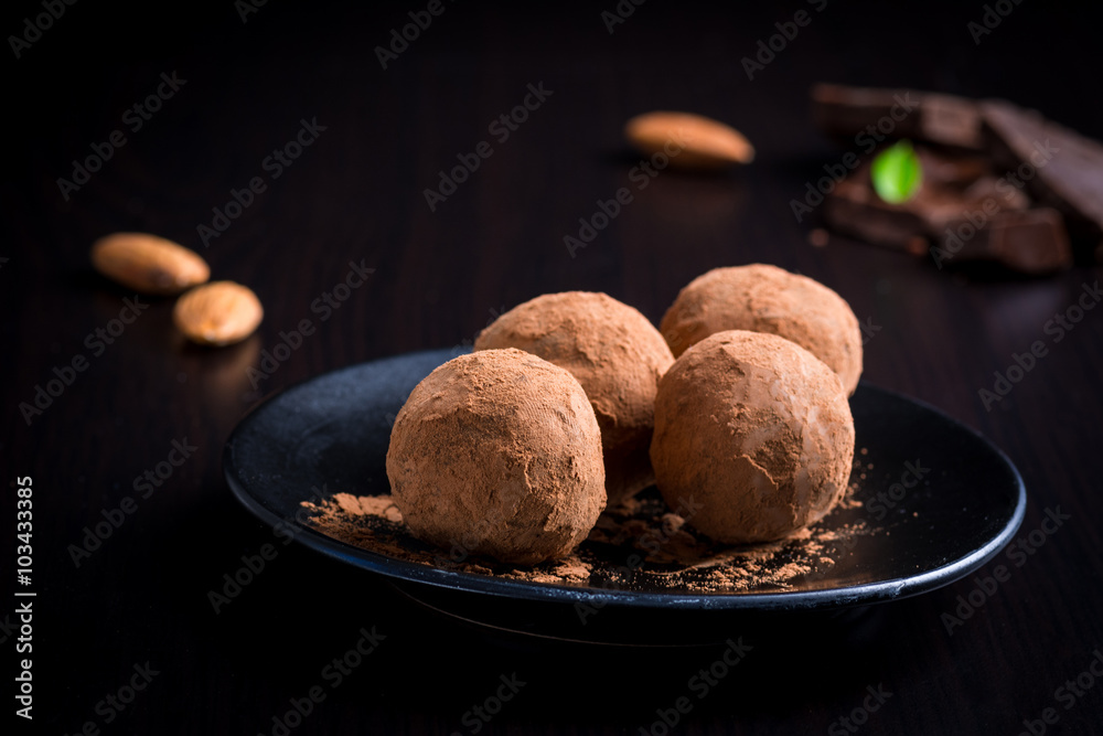 Homemade chocolate truffles on black plate on black background. Luxury dessert, velvety smooth chocolate truffles