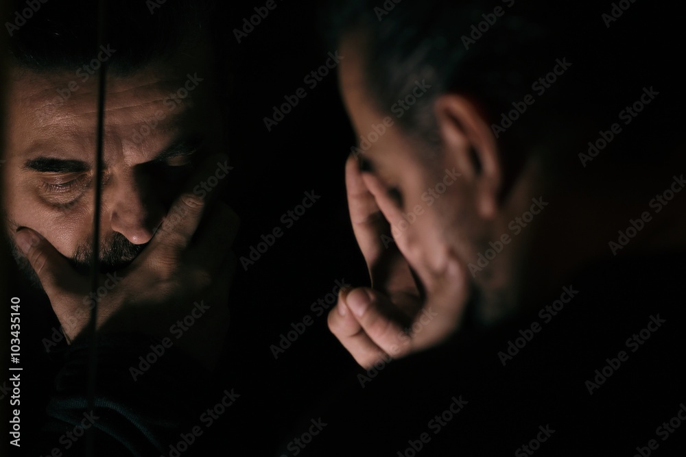 Man in despair, sad and lonely resting his head on a hand, in front of mirror Man in despair, sad and lonely resting his head on a hand, in front of mirror