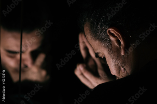 Man in despair, sad and lonely resting his head on a hand, in front of mirror