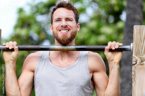 Crossfit fitness man exercising chin-ups workout. Young male adult trainer athlete portrait closeup with hands holding on monkey bars at outdoor gym doing a chin-up strength training muscle exercise.