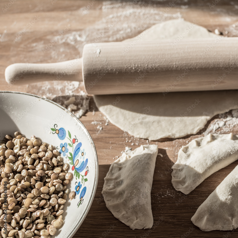 Ταπετσαρία Traditional polish dumplings  - lentil filling in folk bowl, rolling pin and dough on breadboard
