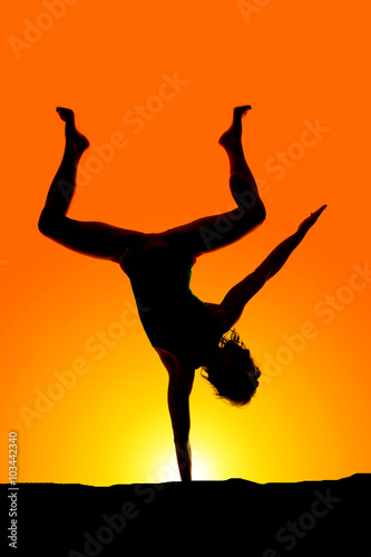 silhouette of a woman on one hand legs up and apart in the sunse