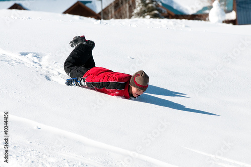 Adorable boy sliding down snow hill on body