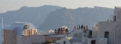  Tourists on Oia  roof tops looking at view and taking photos Island of Thirassia in background. photo