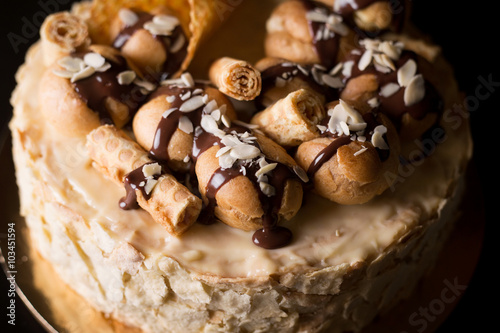 Napoleon cake on a dark wooden background decorated with petals of almonds eclairs, waffles and chocolate icing