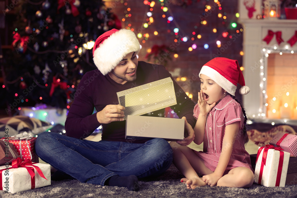 Older brother and little sister in Santa hat opening gift on Christmas background