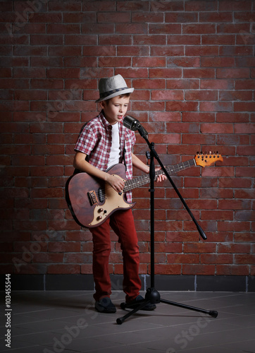 Little boy playing guitar and singing with microphone on a brick wall background photo