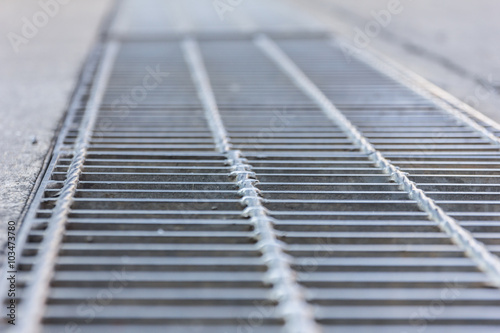 Black and white close up of a sidewalk subway grate with shallow