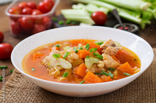 Tomato chicken soup with pumpkin, beans and celery in white bowl