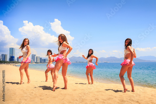 cheerleaders dance one hand aside on beach against resort