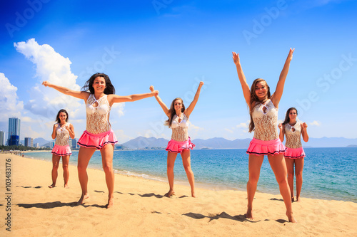 cheerleaders dance differently on beach against azure sea