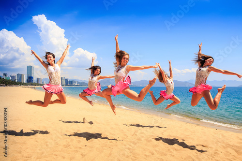 cheerleaders jump in Scales at once on beach against sea